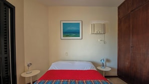 A room with a bed, a small bedside table, a wall-mounted heater, and a wardrobe. - Apto no Guaruja com vista mar a 300m da Praia (Guarujá)
