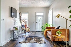 Ein modernes Wohnzimmer mit einer Couch, einem Sessel, einem Fernseher und einem großen Fenster.