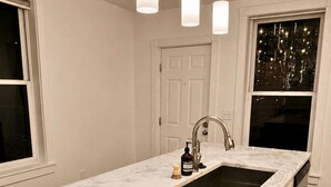 Una cucina con un piano di lavoro in marmo bianco, un lavello in acciaio inossidabile e illuminazione a sospensione.
