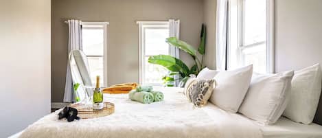 Quarto com cama, janela grande, planta e garrafa de champanhe.