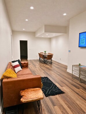 A modern living room with a brown leather sofa, a dining table with chairs, and a black rug. - Cozy Cabana by Jungle House | Downtown & Short North | Free Parking | Near Convention Center & OSU (Columbus)