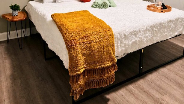Un letto rifatto con lenzuola bianche, un cuscino rosso e una coperta gialla senape.