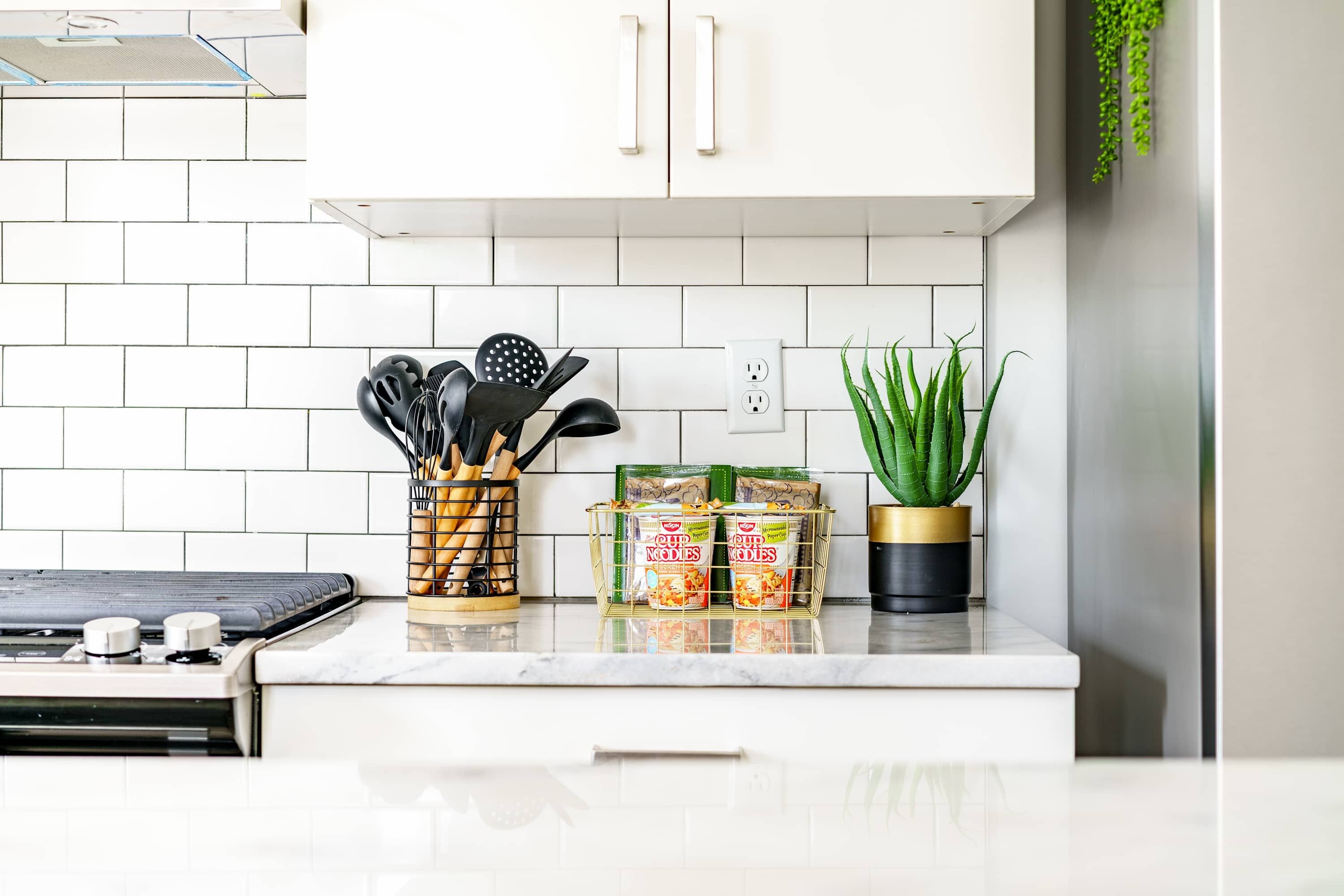 A kitchen with white cabinets, a countertop with a coffee maker, a plant, and packaged food items.