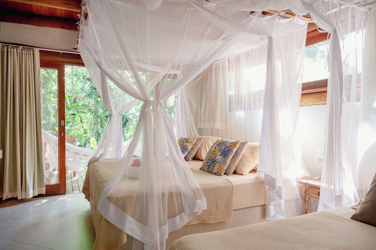 Ein Schlafzimmer mit Baldachinbett und Blick auf grüne Natur, sowie einer Hängematte.