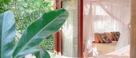 A room with a bed, a window with curtains, and a view of greenery outside.