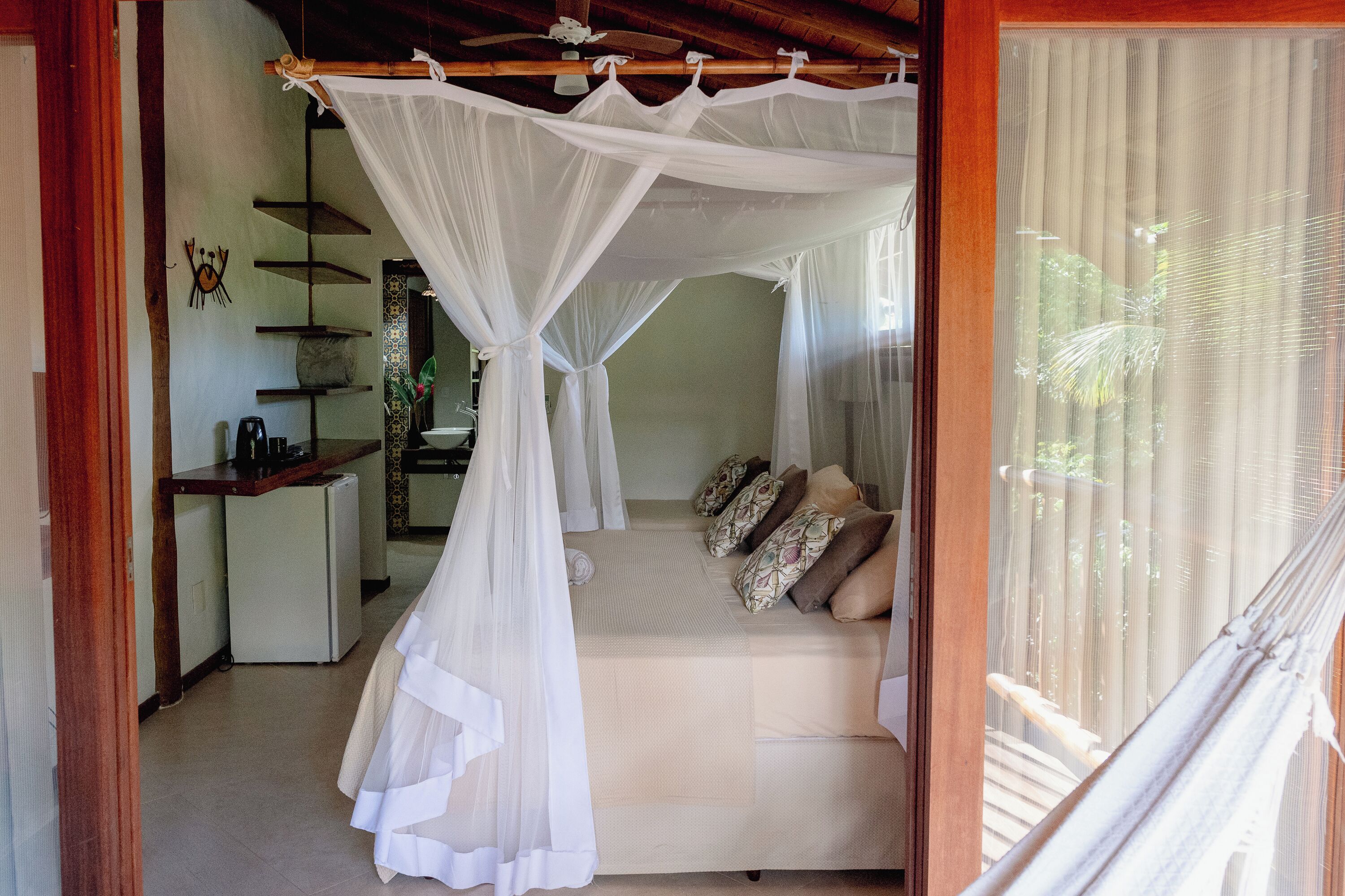 A room with a bed under a canopy, a small kitchenette, and a view of the outdoors.