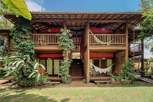 Una casa de madera con un balcón, una hamaca y una escalera que conduce al nivel superior.