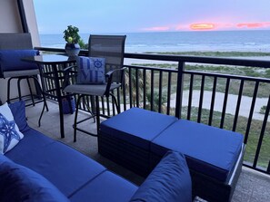 En balkon med udsigt over havet, med en sofa, stole og et lille bord.