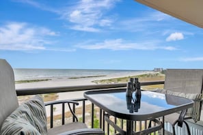 A balcony with a table and chairs, overlooking a beach and ocean. - Million Dollar Gulf View-2 Bed 2 Bath (Clearwater)