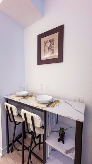 Un comedor con una mesa de mármol, dos sillas, un cuadro en la pared y una planta pequeña en el estante inferior.