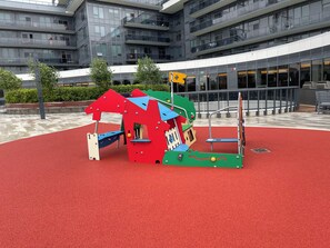 Ein Spielplatz mit roter Bodenfläche und bunten Spielgeräten.