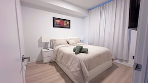 A bedroom with a bed, nightstand, lamp, and a painting on the wall.