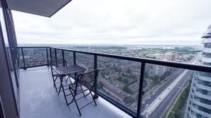 Un balcón con mesa y sillas, con vista a un paisaje urbano de edificios y calles.