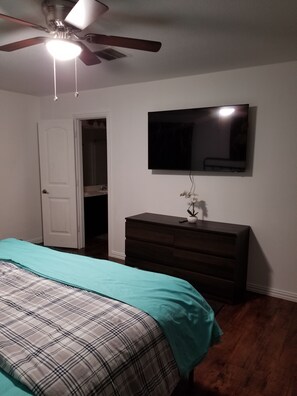 Ein Schlafzimmer mit einem Bett, einem Schminktisch, einem Fernseher und einem Deckenventilator.