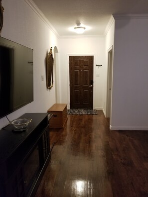 Un couloir avec un plancher en bois, un téléviseur posé sur un meuble, une porte et un miroir accroché au mur.