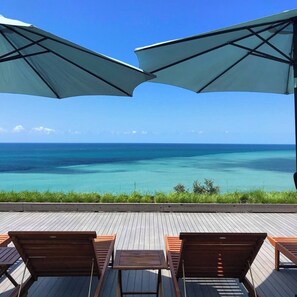 A wooden deck with lounge chairs and umbrellas overlooking a clear blue ocean.