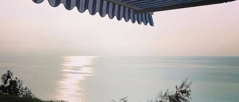 Una terraza con vista al mar, un toldo a rayas y dos sillas.