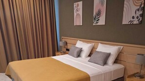 A hotel room with a large bed, a wooden headboard, a nightstand, and a wall with three framed artworks. - Mandrati Loft Room 06 | Sea View Balcony, Heated Pool & Breakfast (Sarpi)
