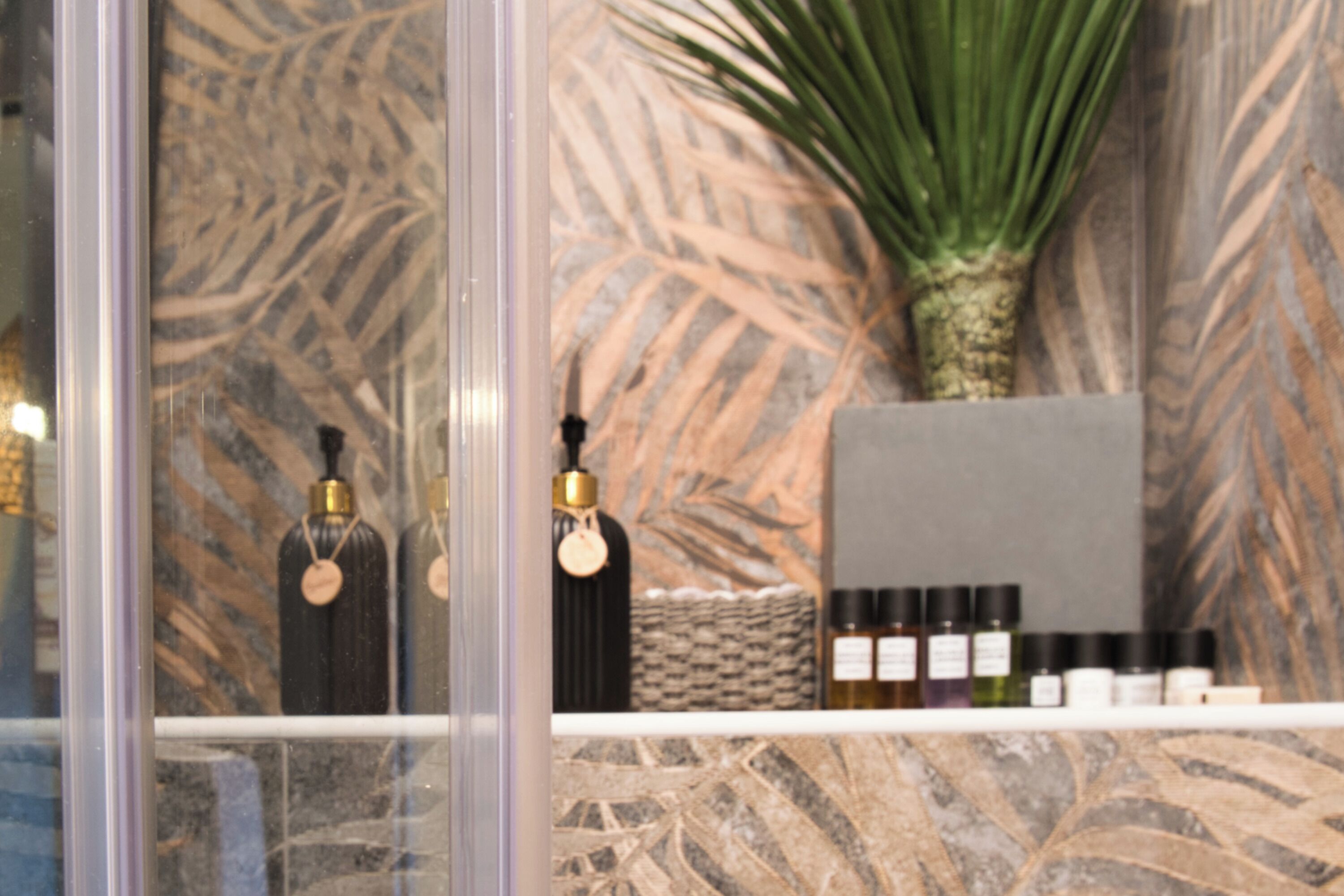 Un baño con pared de mármol, una planta de palma y artículos de tocador en un estante.