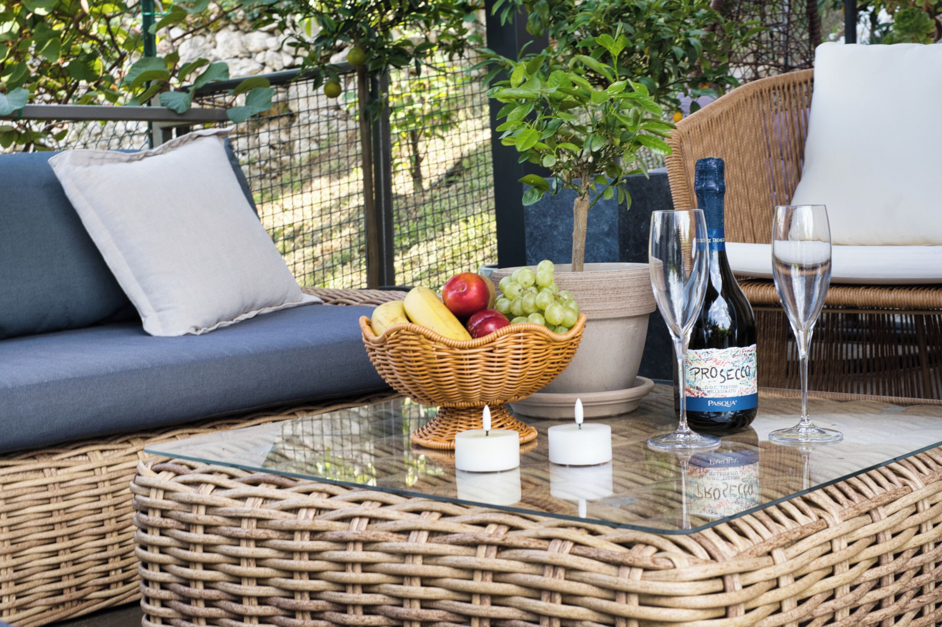 A wicker table with a fruit basket, candles, and wine glasses.