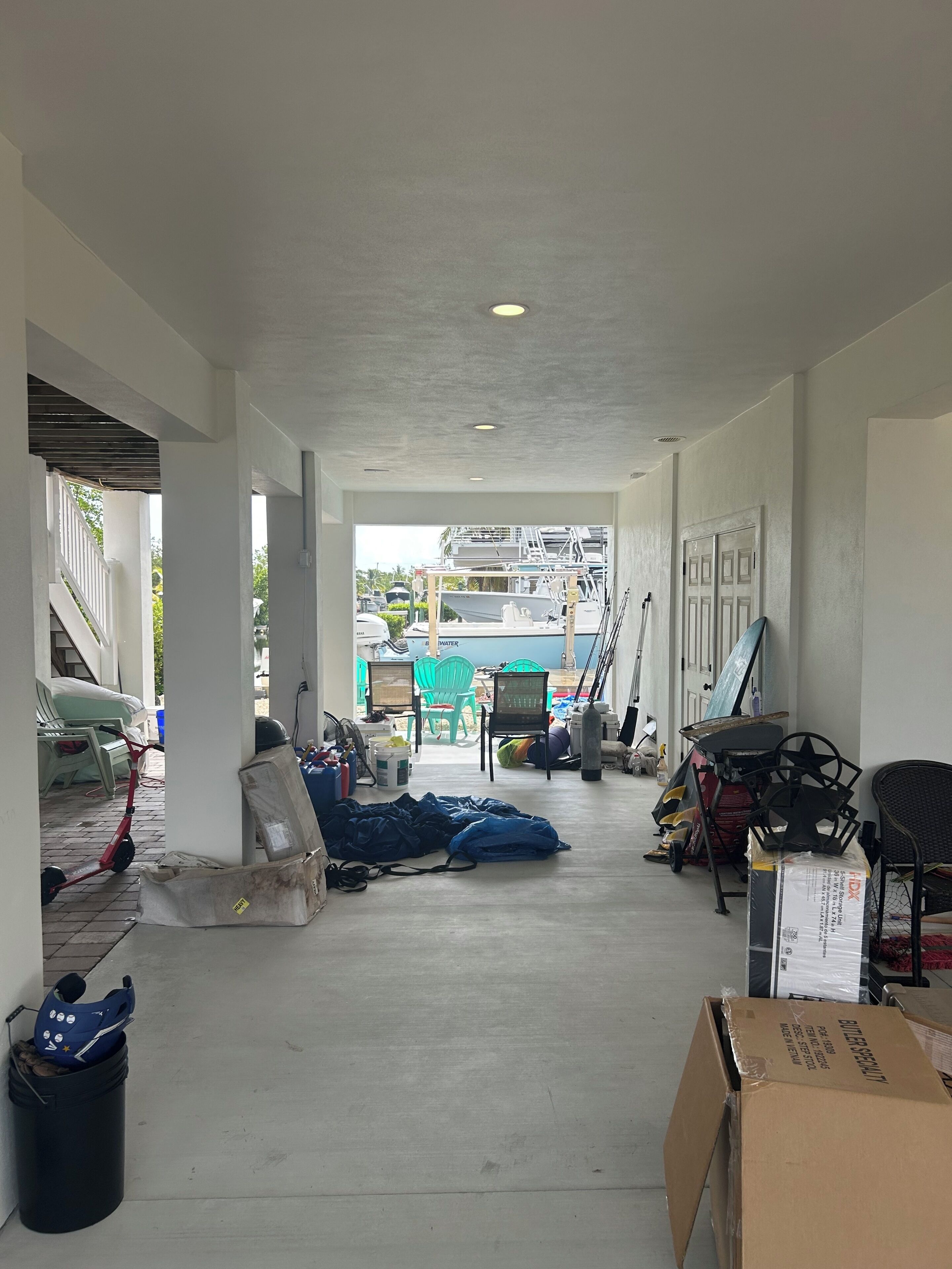 A covered outdoor area with a concrete floor, white walls, and a view of boats in the background.