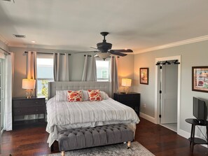 A bedroom with a bed, bedside lamps, a ceiling fan, a window with curtains, and a door. - New 4 bed 3 bath house on Ramrod Key (Ramrod Key)
