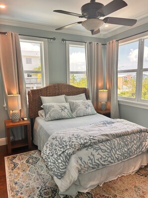 A bedroom with a bed, a ceiling fan, a nightstand with a lamp, and a view of the outside through large windows. - New 4 bed 3 bath house on Ramrod Key (Ramrod Key)