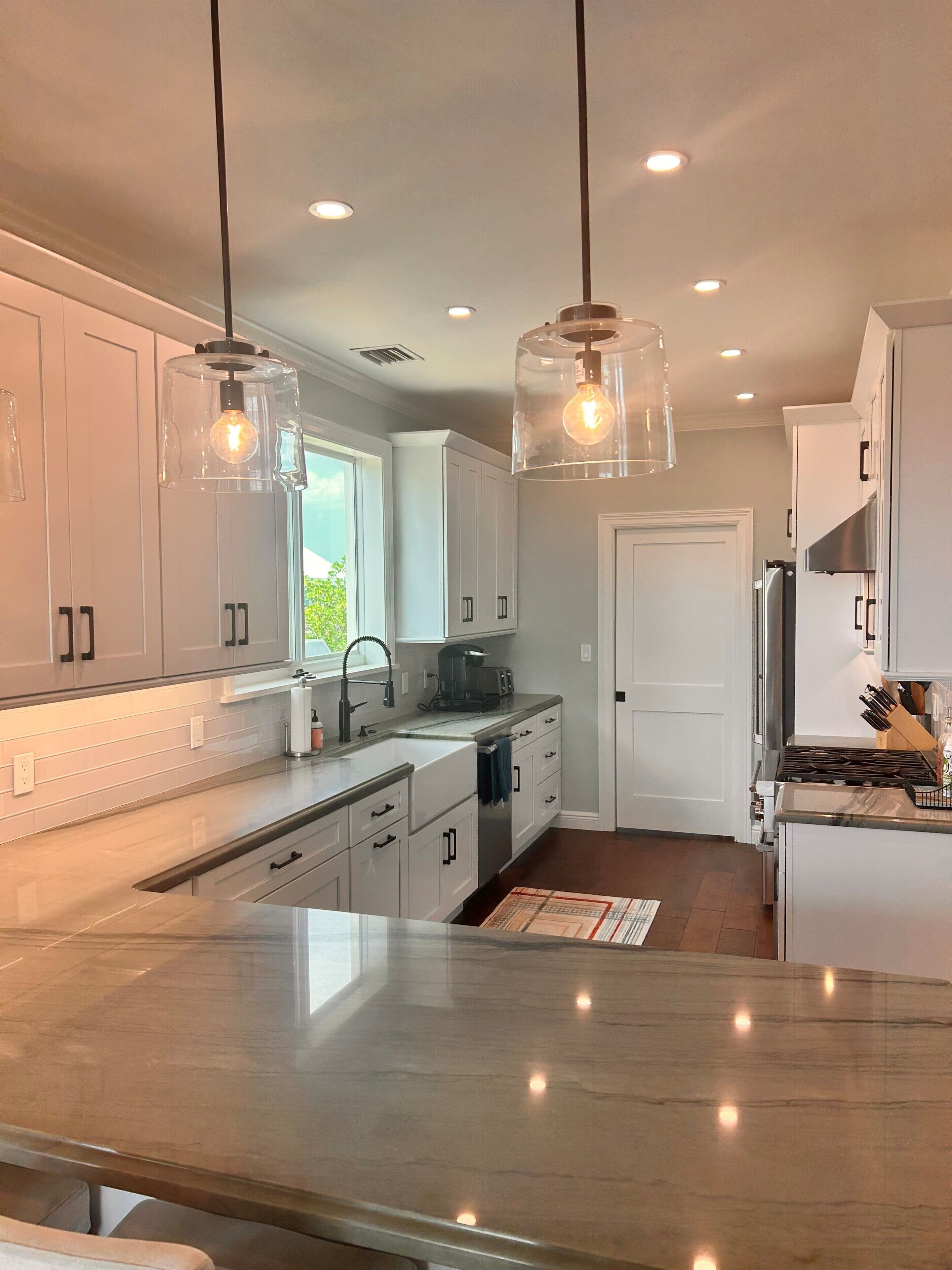 A modern kitchen with white cabinets, a marble countertop, and pendant lighting.