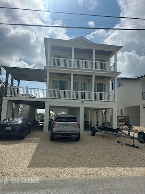 A multi-story building with a covered parking area, two cars, and a visible staircase leading to an upper level. - New 4 bed 3 bath house on Ramrod Key (Ramrod Key)