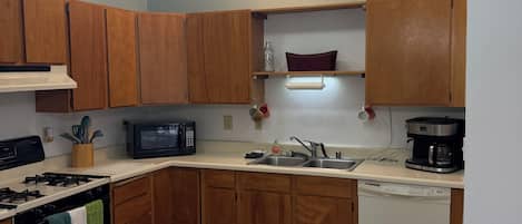 Una cocina con armarios de madera, una estufa, un microondas, un fregadero y un lavavajillas. Hay una mesa de comedor con sillas.