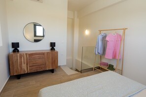 A bedroom with a bed, a wooden dresser, a round mirror, and a clothing rack.