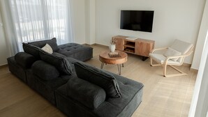 A modern living room with a sectional sofa, a wooden coffee table, a white armchair, and a flat-screen TV mounted on the wall.