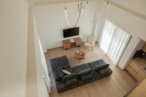 A modern living room with a sectional sofa, a wooden coffee table, a flat-screen TV, and a chair. - Forestbreeze 2: Luxury 1 bedroom villa (Larisos)