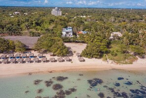 An aerial view of a beach resort with a sandy beach, thatched-roof lounge chairs, and a building with a blue roof. - Vista Marina Beach (Playa Juan Dolio)