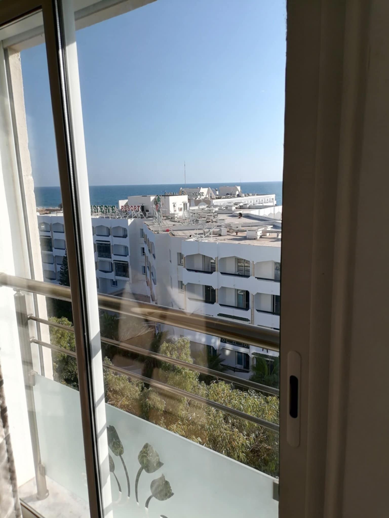 A view from a balcony with a clear sky, overlooking a coastal area with buildings and a resort.