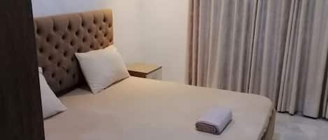 A hotel room with a large bed, a bedside table, an air conditioning unit, and a curtain.