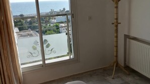 Une chambre avec une grande fenêtre, un lit, un radiateur et un porte-manteau en bois.
