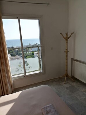 Ein Schlafzimmer mit großem Fenster, einem Bett, einem Heizkörper und einem Holz-Kleiderständer.