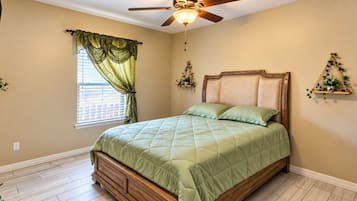 Une chambre à coucher comprenant un lit, un ventilateur de plafond, une fenêtre avec des rideaux et des étagères murales pour les plantes.