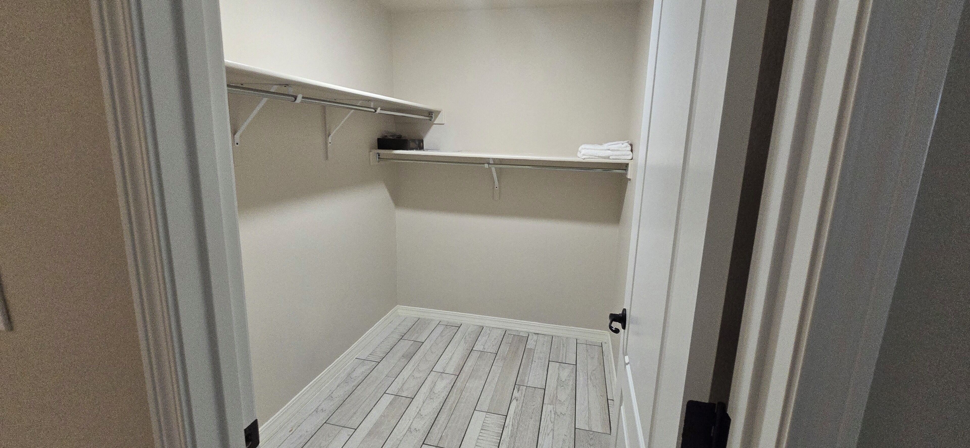 A walk-in closet with a wooden floor, white walls, and shelves with folded towels.