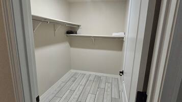 A walk-in closet with a wooden floor, white walls, and shelves with folded towels.