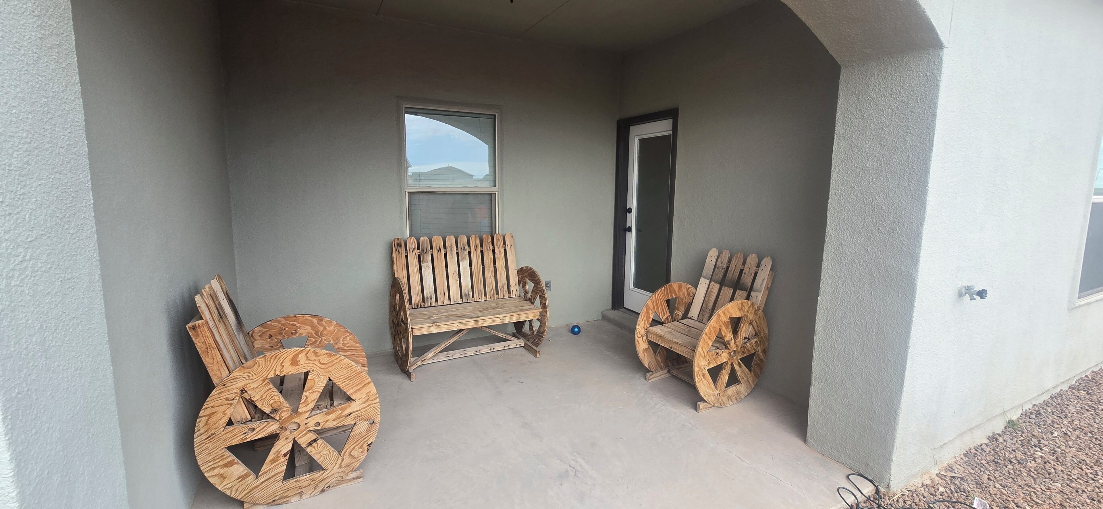 Une véranda couverte avec deux chaises en bois et une grande roue en bois.