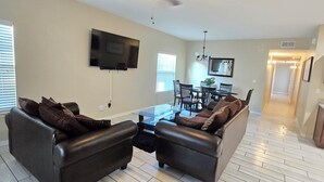 A living room with a sofa set, a coffee table, and a flat-screen TV mounted on the wall.