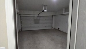 A garage with a closed garage door, a ceiling-mounted light fixture, and a concrete floor.