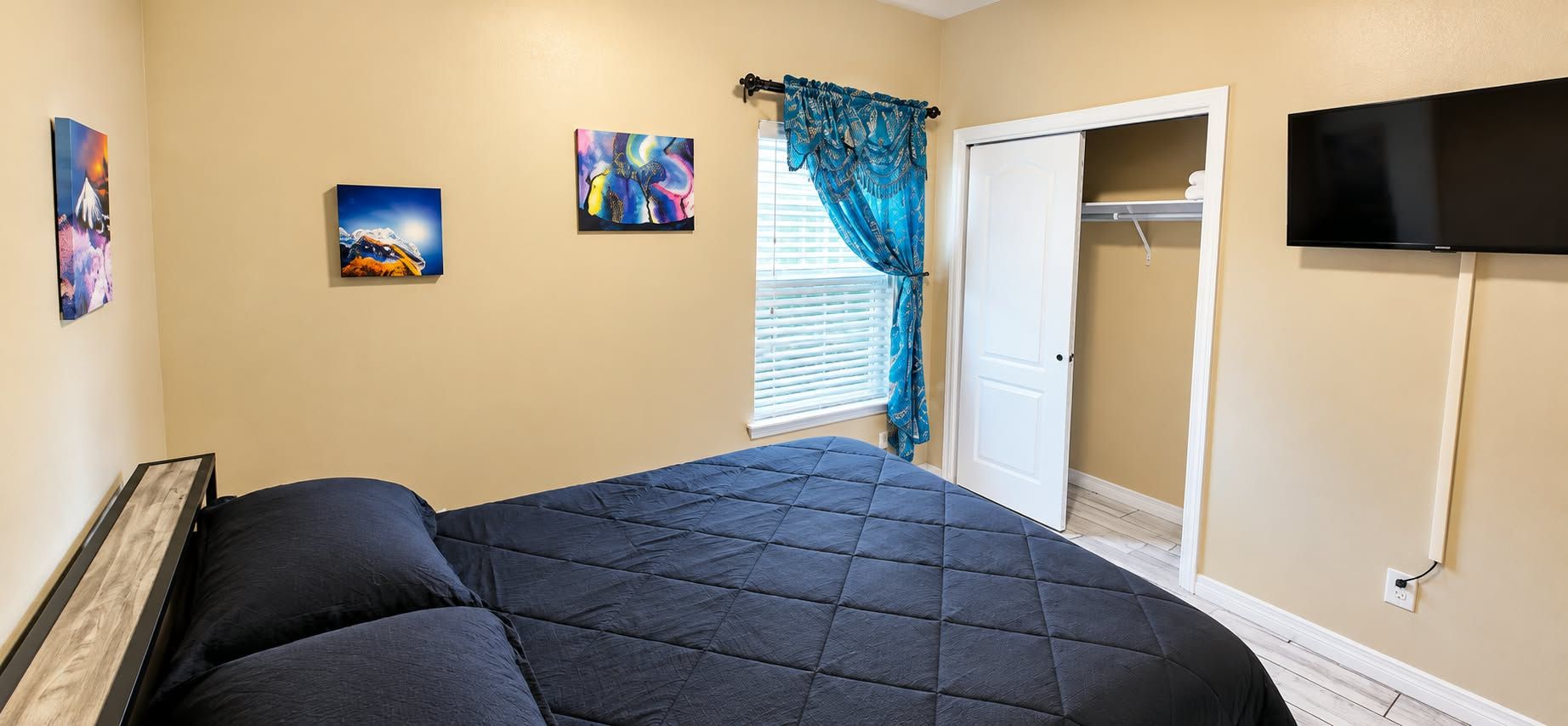 A bedroom with a bed, a TV, and artwork on the wall.