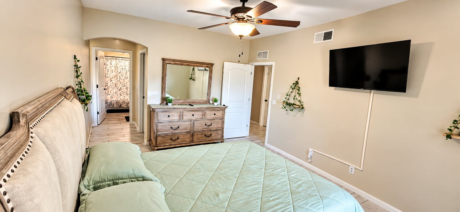 Un dormitorio con cama, cómoda, espejo, ventilador de techo y televisión.