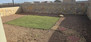 A backyard with a square area of artificial grass, surrounded by a stone wall and gravel ground.