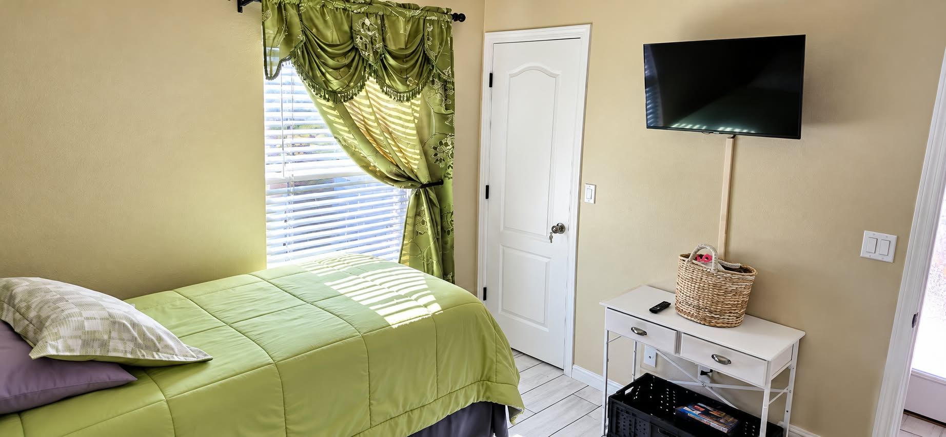 A bedroom with a bed, a television, a desk, and a window with curtains.