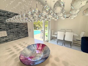 A modern kitchen with a large glass bowl centerpiece, a dining area with white chairs, and a pool visible through the glass doors. - Short Walk to Beach • 3BR Poolside Unit • Next to Nature Preserve (Fort Myers Beach)