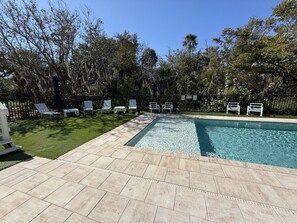 A rectangular swimming pool with a tiled deck in the foreground, surrounded by a grassy area and trees. - Short Walk to Beach • 3BR Poolside Unit • Next to Nature Preserve (Fort Myers Beach)